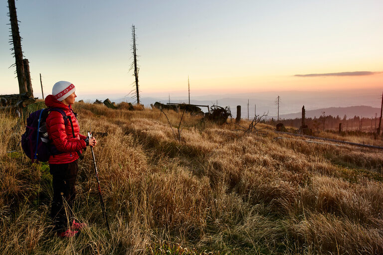Ein Wanderer mit Rucksack blickt auf den Sonnenaufgang im Bayerischen Wald.